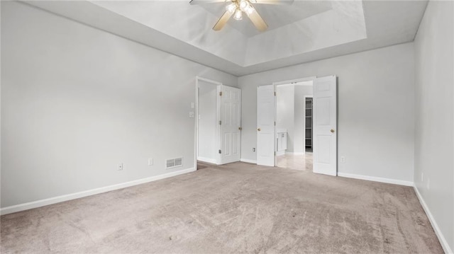 unfurnished bedroom with carpet, a tray ceiling, visible vents, a ceiling fan, and baseboards