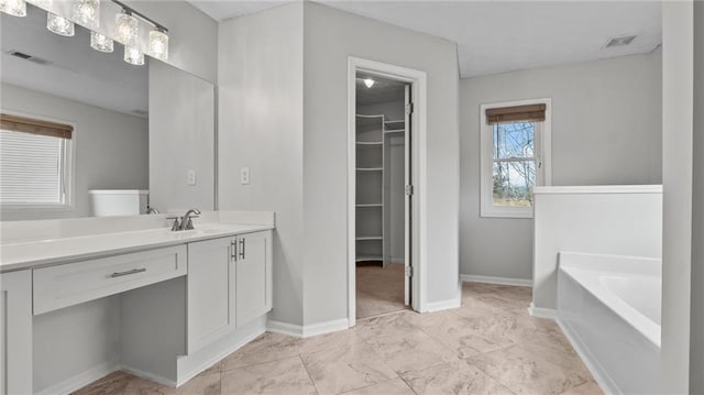 bathroom with baseboards, visible vents, a walk in closet, vanity, and a bath