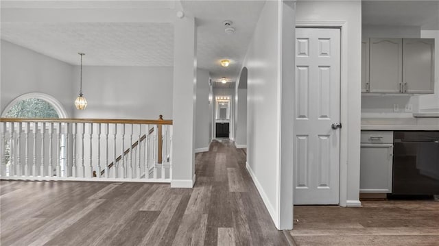 hallway with lofted ceiling, a textured ceiling, an upstairs landing, wood finished floors, and baseboards