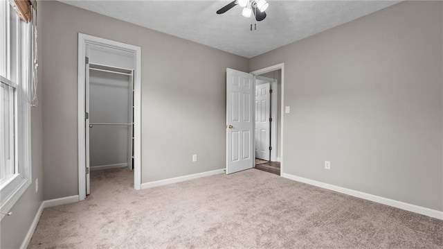 unfurnished bedroom featuring baseboards, ceiling fan, a walk in closet, carpet flooring, and a closet