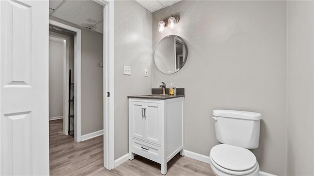 bathroom featuring toilet, baseboards, wood finished floors, and vanity