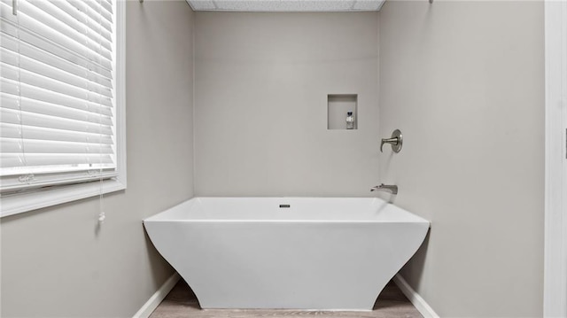 bathroom featuring a soaking tub, wood finished floors, and baseboards