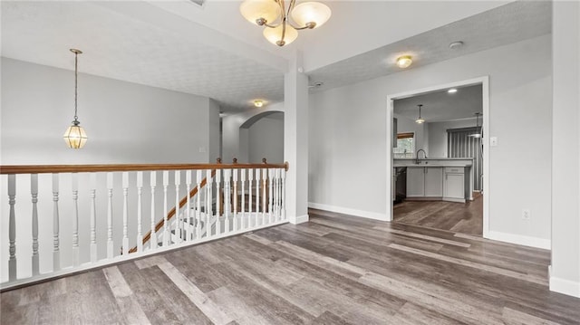 spare room featuring a sink, arched walkways, wood finished floors, and baseboards