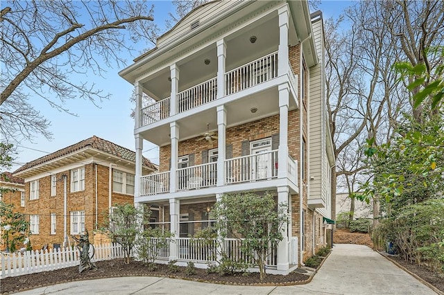 view of front of property with a balcony, ceiling fan, fence, and brick siding