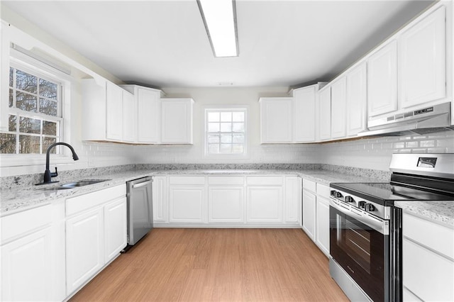 kitchen with light stone countertops, light hardwood / wood-style flooring, stainless steel appliances, white cabinets, and sink