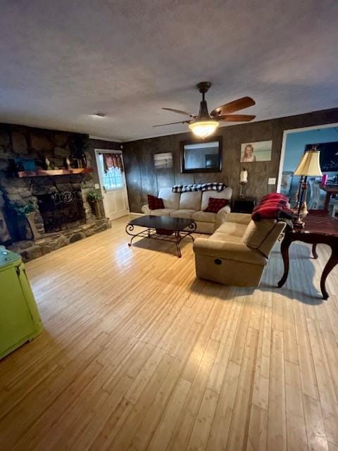 living room featuring ceiling fan, a stone fireplace, and light hardwood / wood-style floors