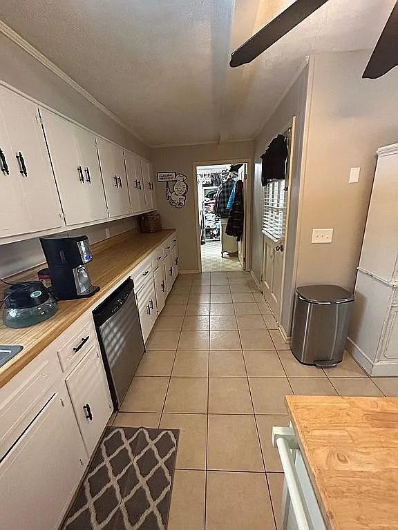 kitchen with wood counters, white cabinetry, a textured ceiling, light tile patterned floors, and stainless steel dishwasher