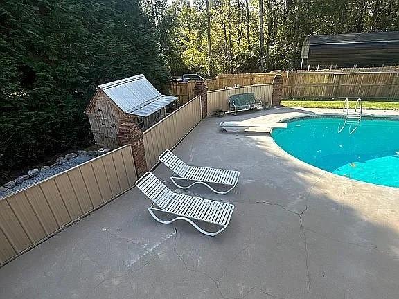 view of swimming pool featuring a storage unit, a diving board, and a patio area