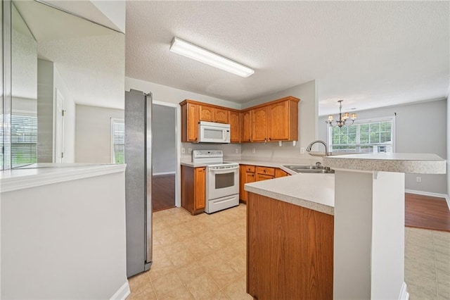 237 Raventree Ln, Griffin, GA 30224 - kitchen featuring white appliances, a peninsula, a chandelier, light countertops, and brown cabinetry