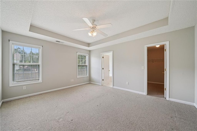 237 Raventree Ln, Griffin, GA 30224 - unfurnished bedroom featuring a textured ceiling, a tray ceiling, carpet, multiple windows, and a walk in closet