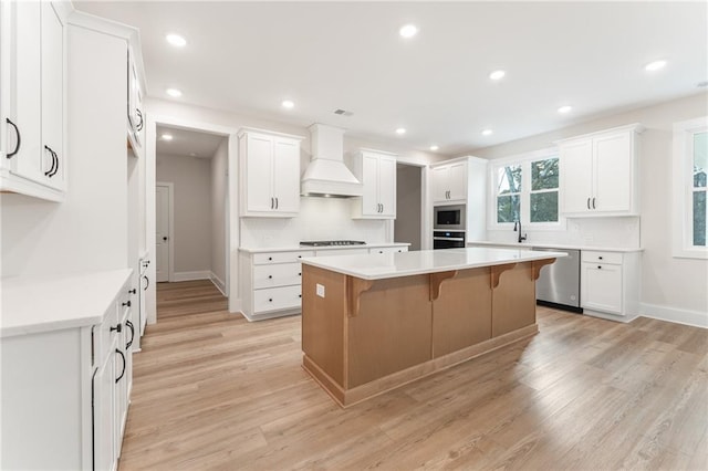 kitchen featuring a breakfast bar, custom range hood, appliances with stainless steel finishes, a kitchen island, and light wood-type flooring