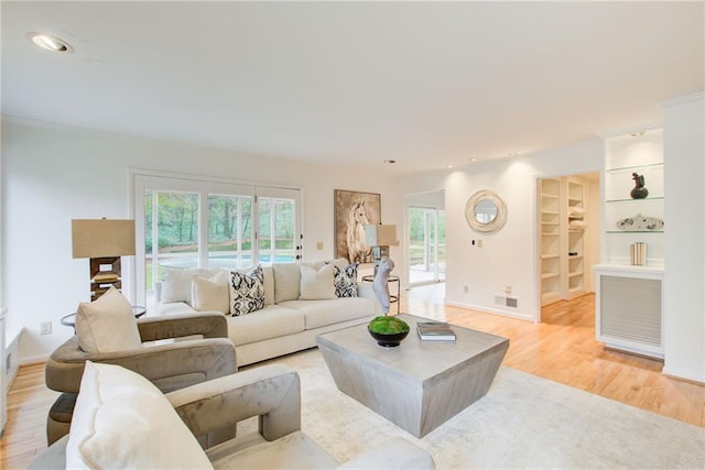 living room featuring ornamental molding, light wood-type flooring, and built in shelves