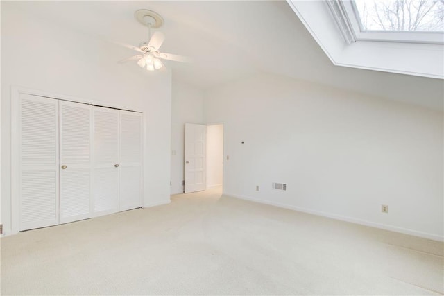 unfurnished bedroom with light carpet, vaulted ceiling with skylight, ceiling fan, and a closet