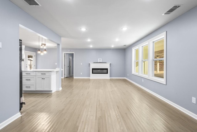 unfurnished living room featuring light wood-type flooring and an inviting chandelier