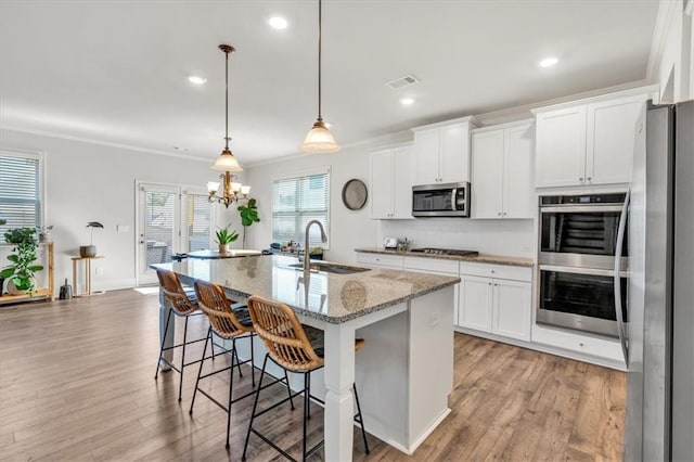 kitchen with crown molding, light stone countertops, a center island with sink, stainless steel appliances, and a sink