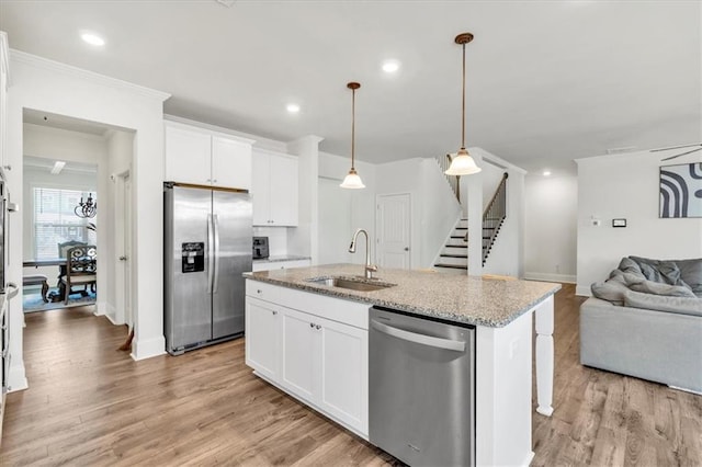 kitchen featuring a sink, open floor plan, appliances with stainless steel finishes, light wood finished floors, and light stone countertops