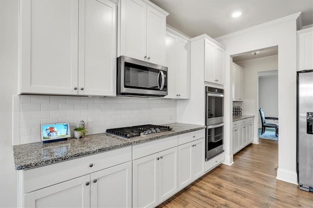 kitchen with light stone counters, white cabinets, appliances with stainless steel finishes, crown molding, and light wood-type flooring