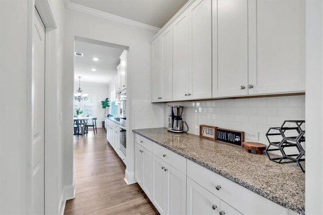 kitchen with light wood-type flooring, light stone counters, backsplash, white cabinets, and crown molding