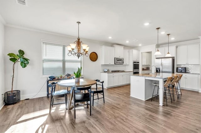 kitchen with ornamental molding, decorative backsplash, stainless steel appliances, light wood-type flooring, and a chandelier