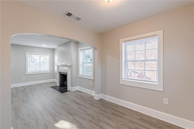 unfurnished living room with a fireplace with flush hearth, visible vents, baseboards, and wood finished floors