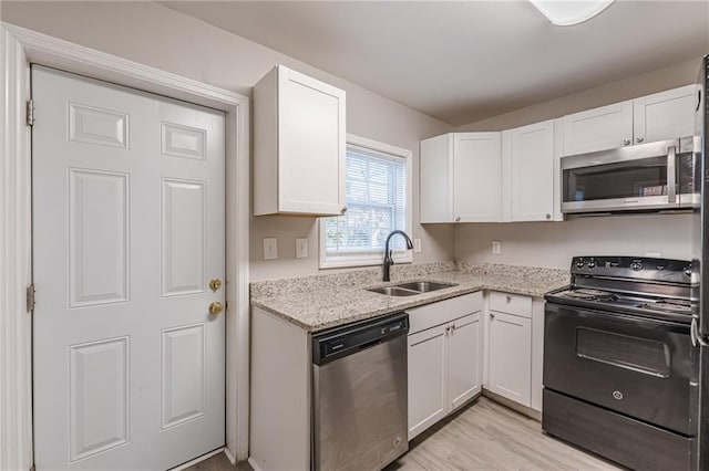 kitchen featuring light stone counters, stainless steel appliances, light wood-style floors, white cabinetry, and a sink