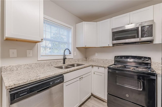 kitchen with stainless steel appliances, a sink, white cabinetry, light wood-type flooring, and light stone countertops