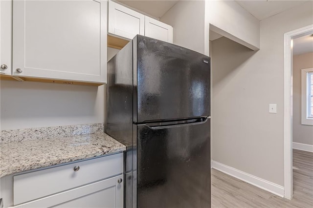 kitchen with light wood finished floors, baseboards, freestanding refrigerator, light stone countertops, and white cabinetry