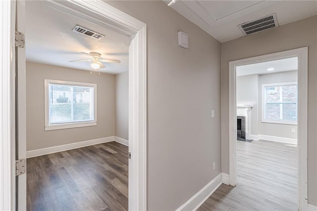 hallway with attic access, wood finished floors, visible vents, and baseboards