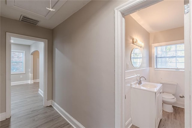 half bath with toilet, visible vents, wood finished floors, and vanity