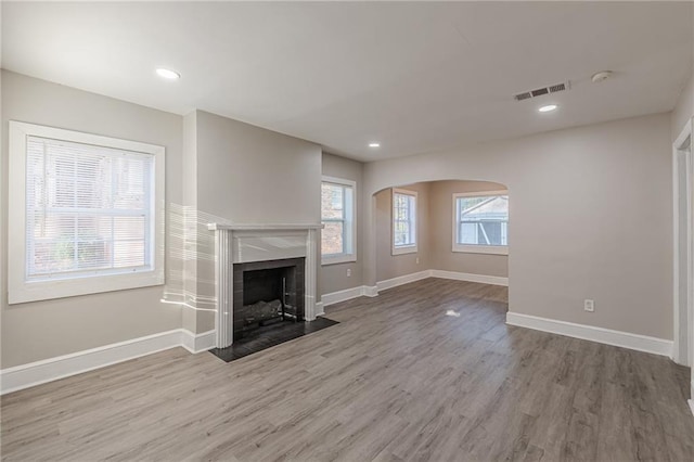 unfurnished living room featuring wood finished floors, a fireplace with flush hearth, visible vents, and baseboards