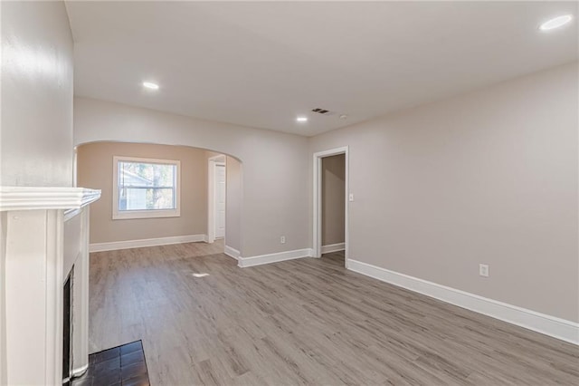 unfurnished living room featuring arched walkways, recessed lighting, a fireplace with flush hearth, wood finished floors, and baseboards