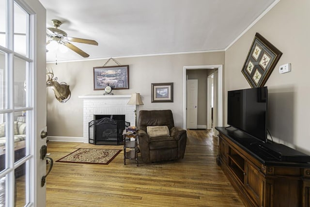 living room featuring hardwood / wood-style flooring, ceiling fan, ornamental molding, and a fireplace