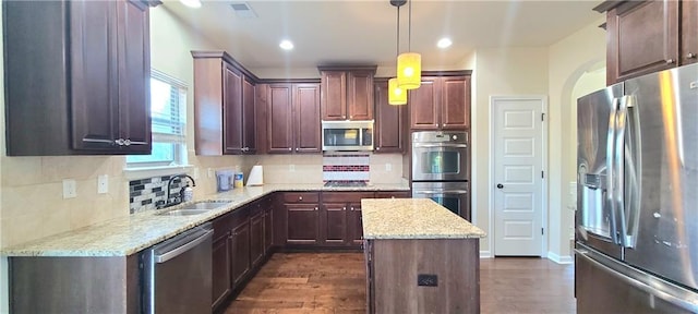 kitchen with dark wood-type flooring, sink, decorative light fixtures, appliances with stainless steel finishes, and a kitchen island