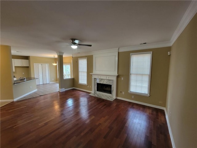 unfurnished living room featuring sink, ornamental molding, dark hardwood / wood-style floors, a premium fireplace, and ceiling fan with notable chandelier