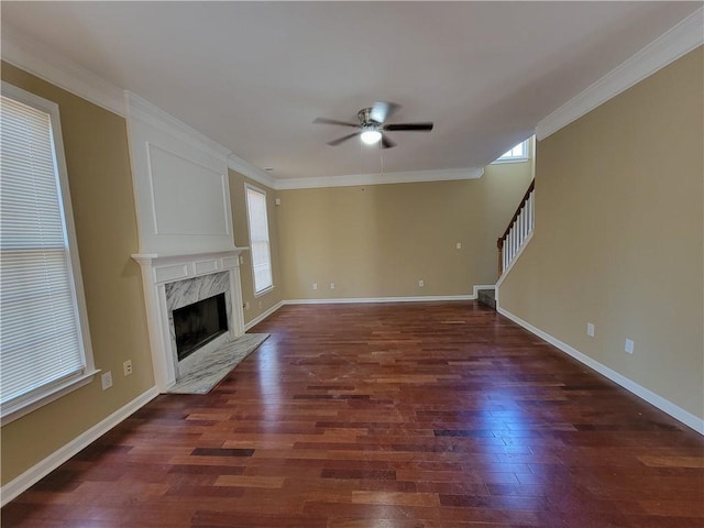 unfurnished living room featuring a premium fireplace, dark wood-type flooring, ceiling fan, and ornamental molding