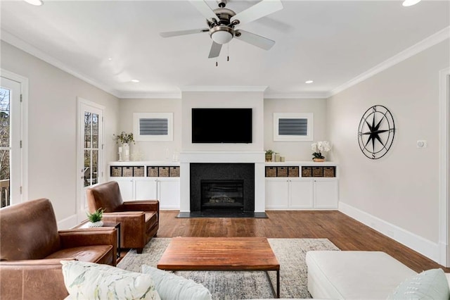 living room featuring a fireplace with flush hearth, crown molding, baseboards, and wood finished floors