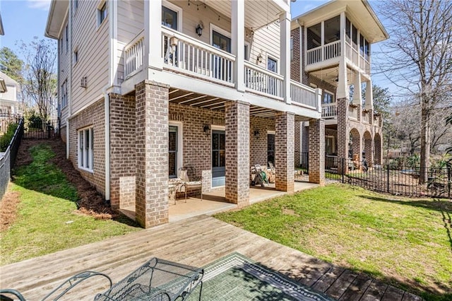 rear view of property with brick siding, a lawn, a fenced backyard, a balcony, and a patio