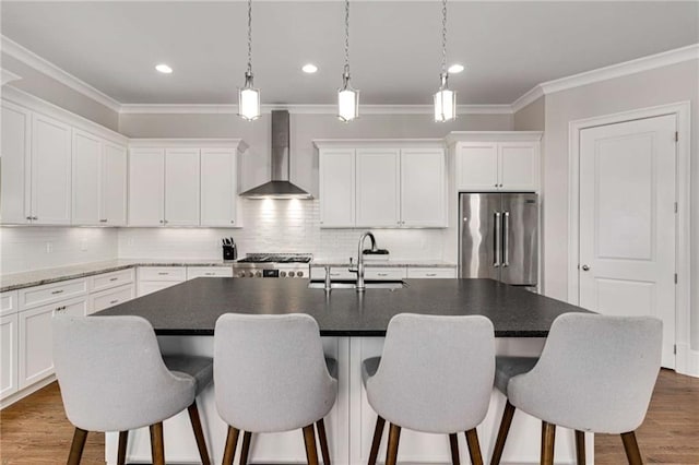 kitchen featuring high end fridge, a kitchen island with sink, a sink, wall chimney range hood, and stove