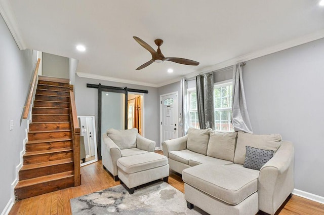 living room featuring light wood finished floors, stairway, a barn door, crown molding, and a ceiling fan