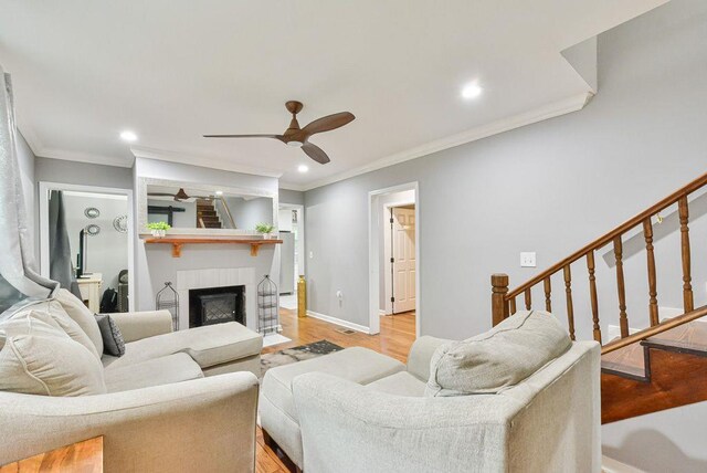 living area featuring a large fireplace, a ceiling fan, light wood-style flooring, and crown molding