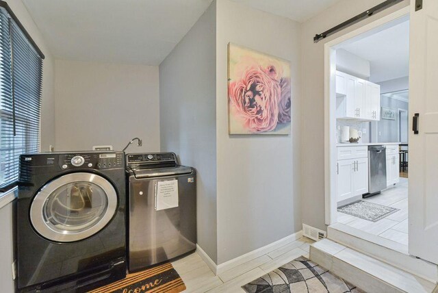clothes washing area with laundry area, a barn door, light tile patterned floors, washing machine and clothes dryer, and baseboards