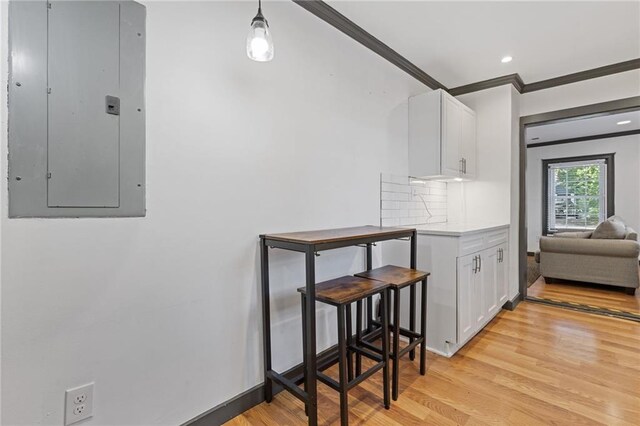 kitchen with tasteful backsplash, light wood-type flooring, electric panel, crown molding, and white cabinets