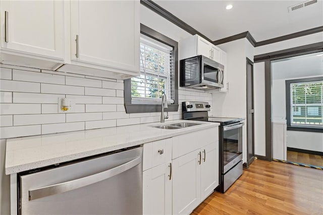 kitchen with white cabinetry, stainless steel appliances, light stone countertops, crown molding, and sink