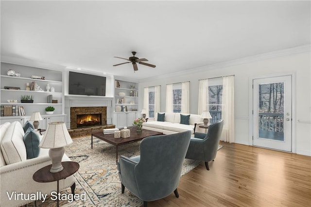 living room featuring ornamental molding, built in features, ceiling fan, and a stone fireplace