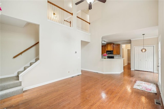 unfurnished living room with a towering ceiling, light hardwood / wood-style flooring, and ceiling fan