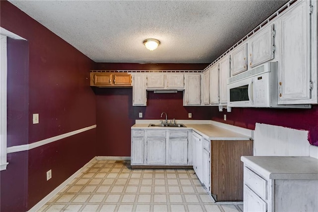 kitchen featuring a textured ceiling, white cabinetry, sink, and white appliances