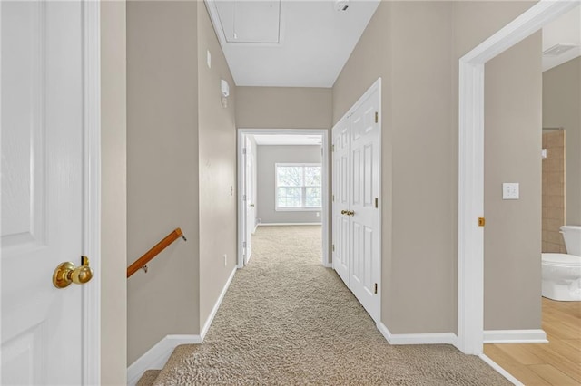 hall featuring baseboards, light carpet, attic access, and an upstairs landing