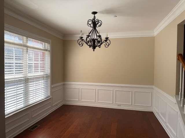 unfurnished dining area featuring a healthy amount of sunlight, an inviting chandelier, ornamental molding, and dark wood-type flooring