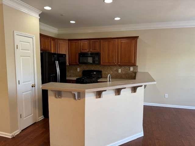 kitchen featuring tasteful backsplash, black appliances, a peninsula, dark wood-style floors, and a breakfast bar