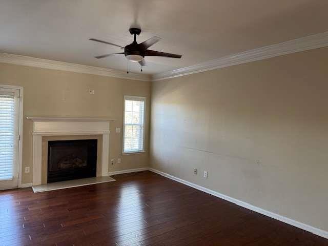 unfurnished living room with ornamental molding, wood finished floors, baseboards, a fireplace with raised hearth, and a ceiling fan